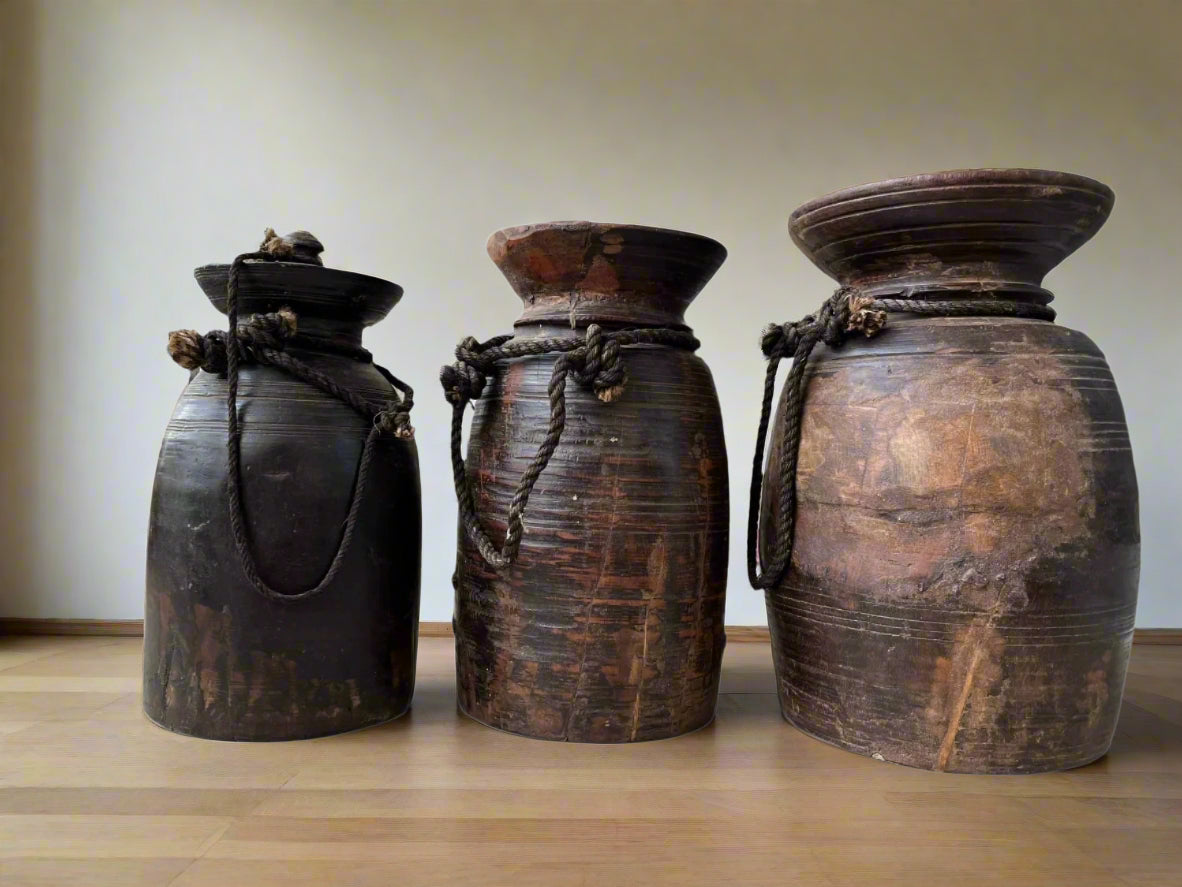 A hand-carved, vintage, rustic Himalayan pot made of teakwood with a rope handle, showing natural wear and age.