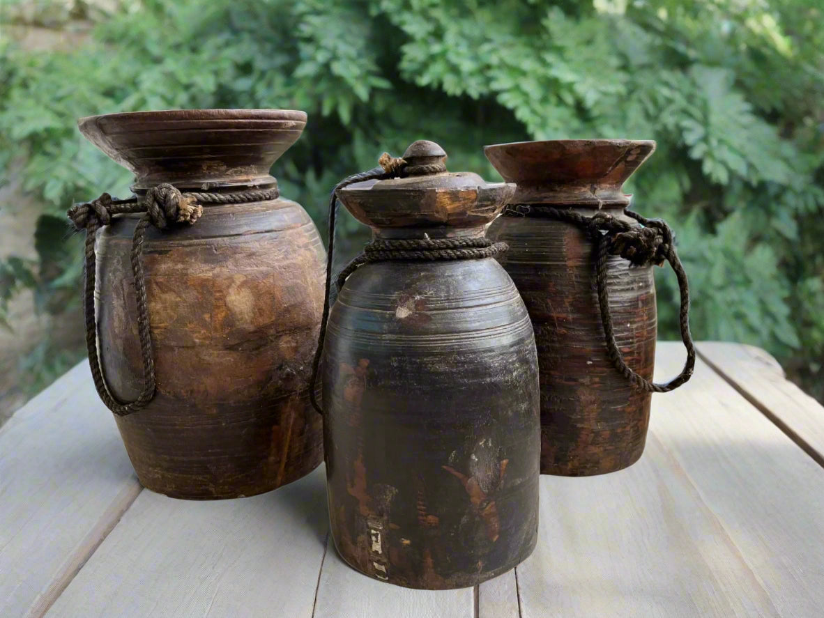 Three vintage Himalayan pots made of teakwood, featuring rustic designs and weathering, bound with ropes.