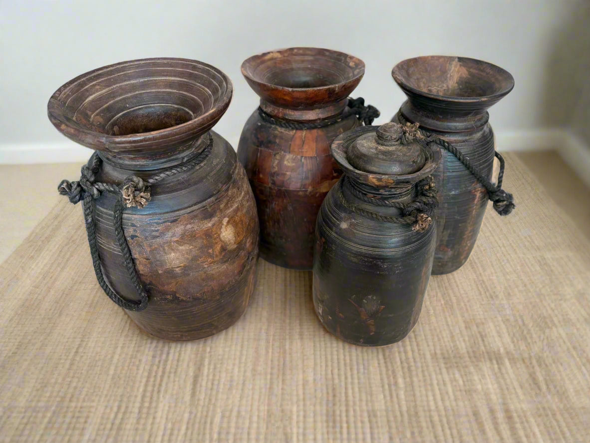 A hand-carved, vintage, rustic Himalayan pot made of teakwood with a rope handle, showing natural wear and age.