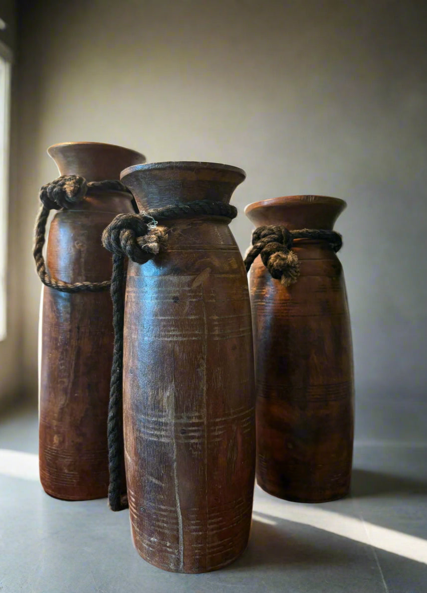 Three rustic wooden vases with rope handles on a wooden surface.