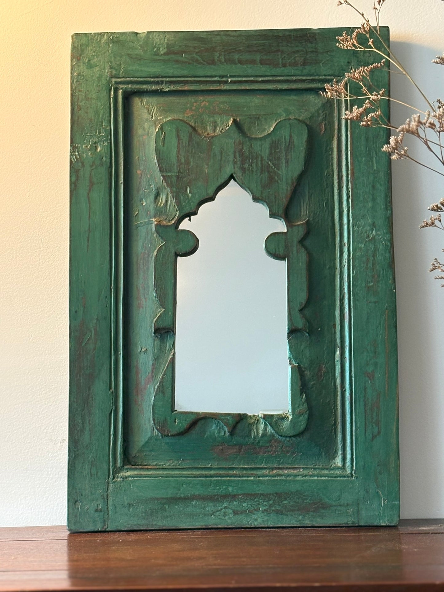 Decorative vintage green mirror with intricate carvings on a wooden surface.