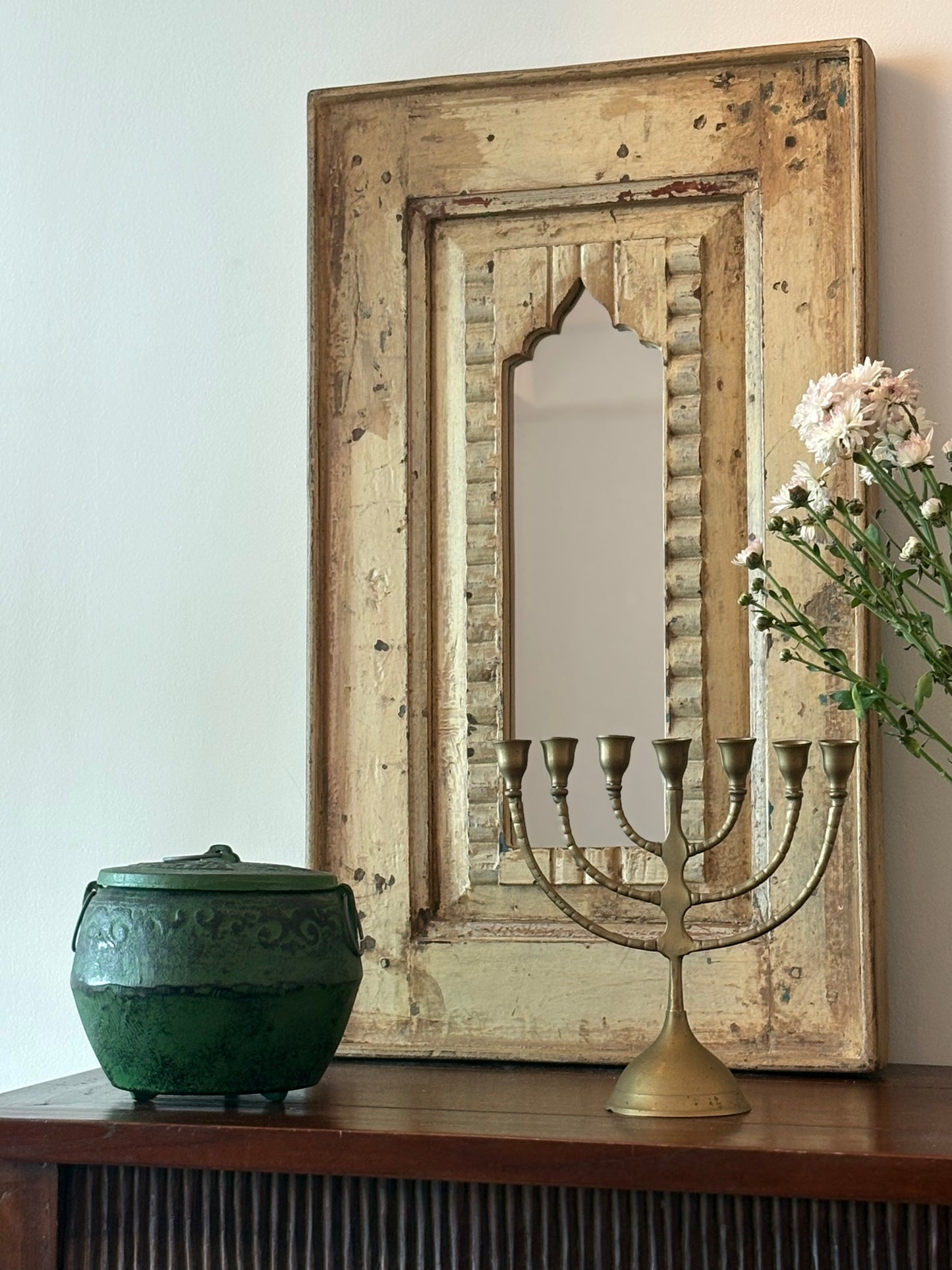 Decorative mirror with wooden frame, green ceramic pot, and brass candelabra on a wooden surface.