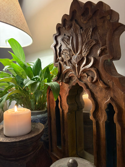 Decorative wooden mirror with intricate carvings next to a potted plant and candle.