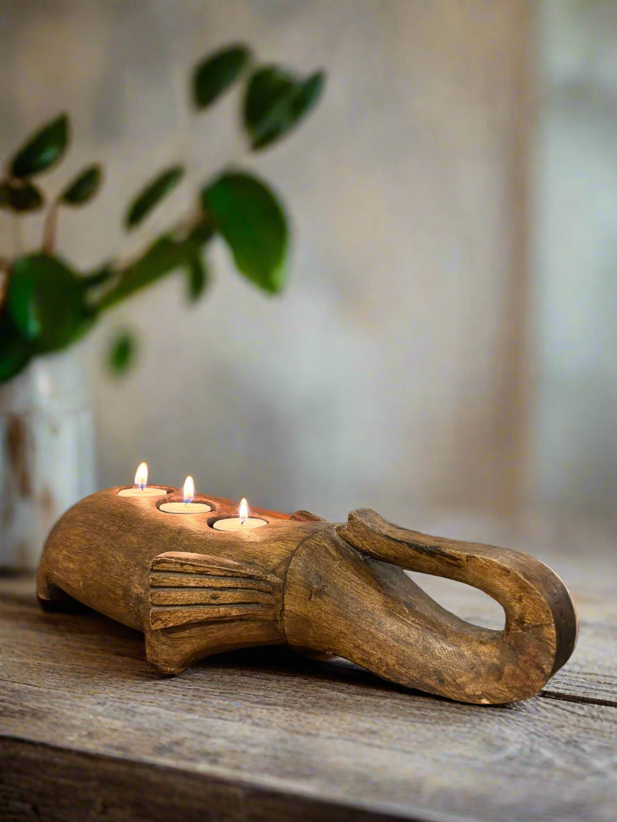 Wooden candle holder shaped like a elephant with three candles on a wooden surface.