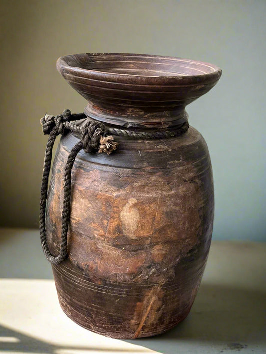 A hand-carved, vintage, rustic Himalayan  pot made of teakwood with a rope handle, showing natural wear and age.