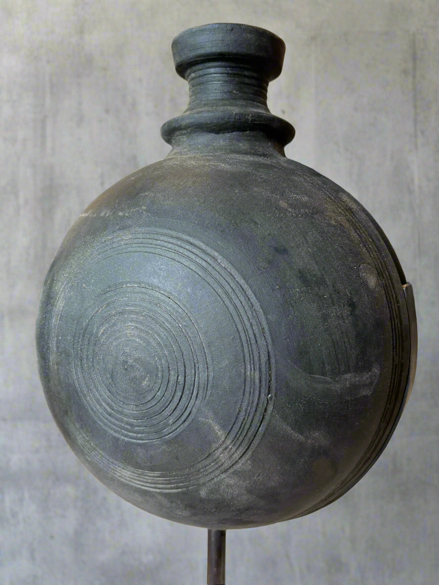 Black handmade clay pot with textured surface on a stand indoors