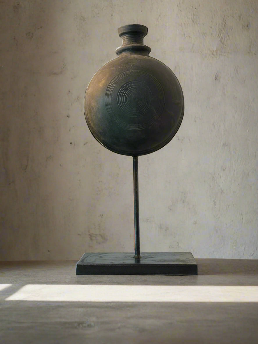 Handmade black pot on a stand against a neutral background