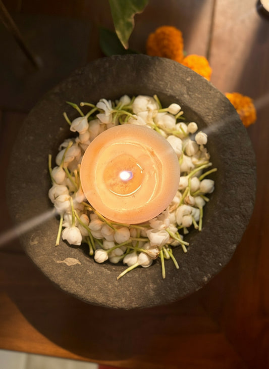 Candle in a stone bowl with flowers on a dark surface