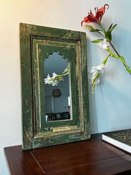 A vintage teakwood mirror with a green frame, hanging on a wall.