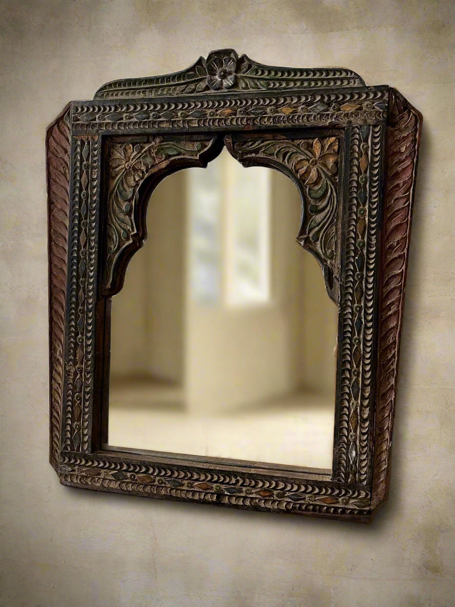 An antique hand-carved wooden mirror with a floral pattern and a brown finish, showing signs of weathering and age.