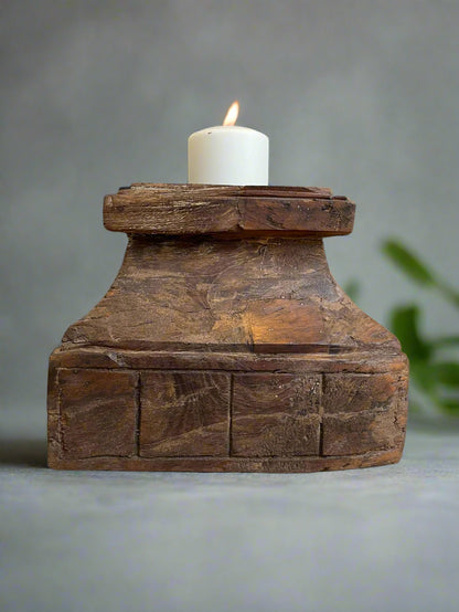 An antique teakwood candle holder with a lit candle on top, displaying natural cracks and an aged patina.