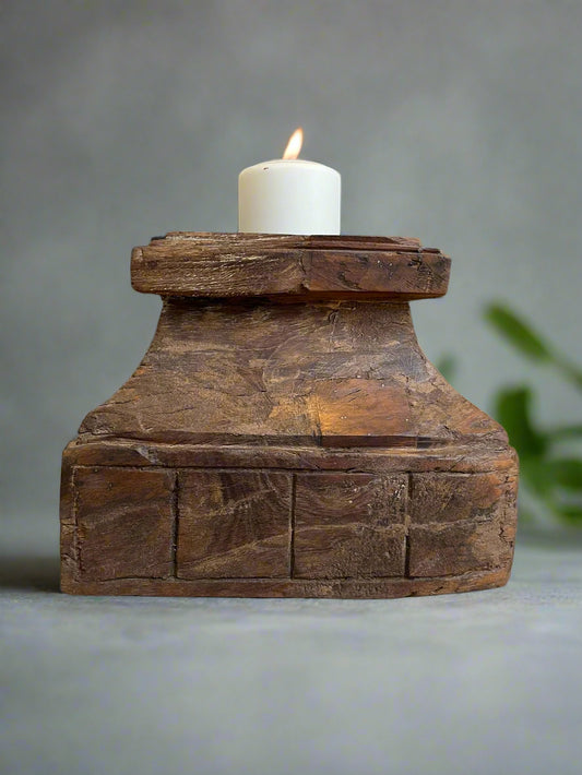 An antique teakwood candle holder with a lit candle on top, displaying natural cracks and an aged patina.