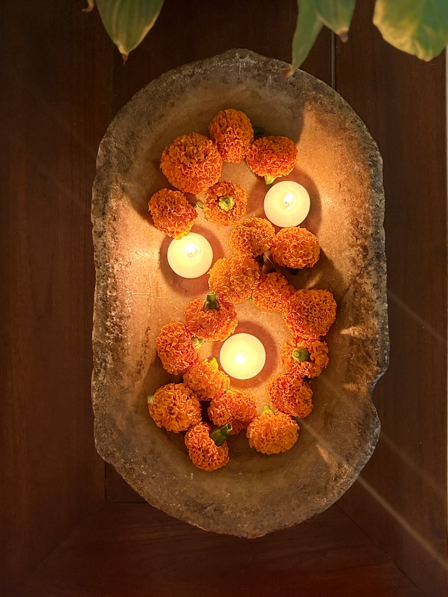 Decorative arrangement of marigold flowers and candles in a stone bowl.