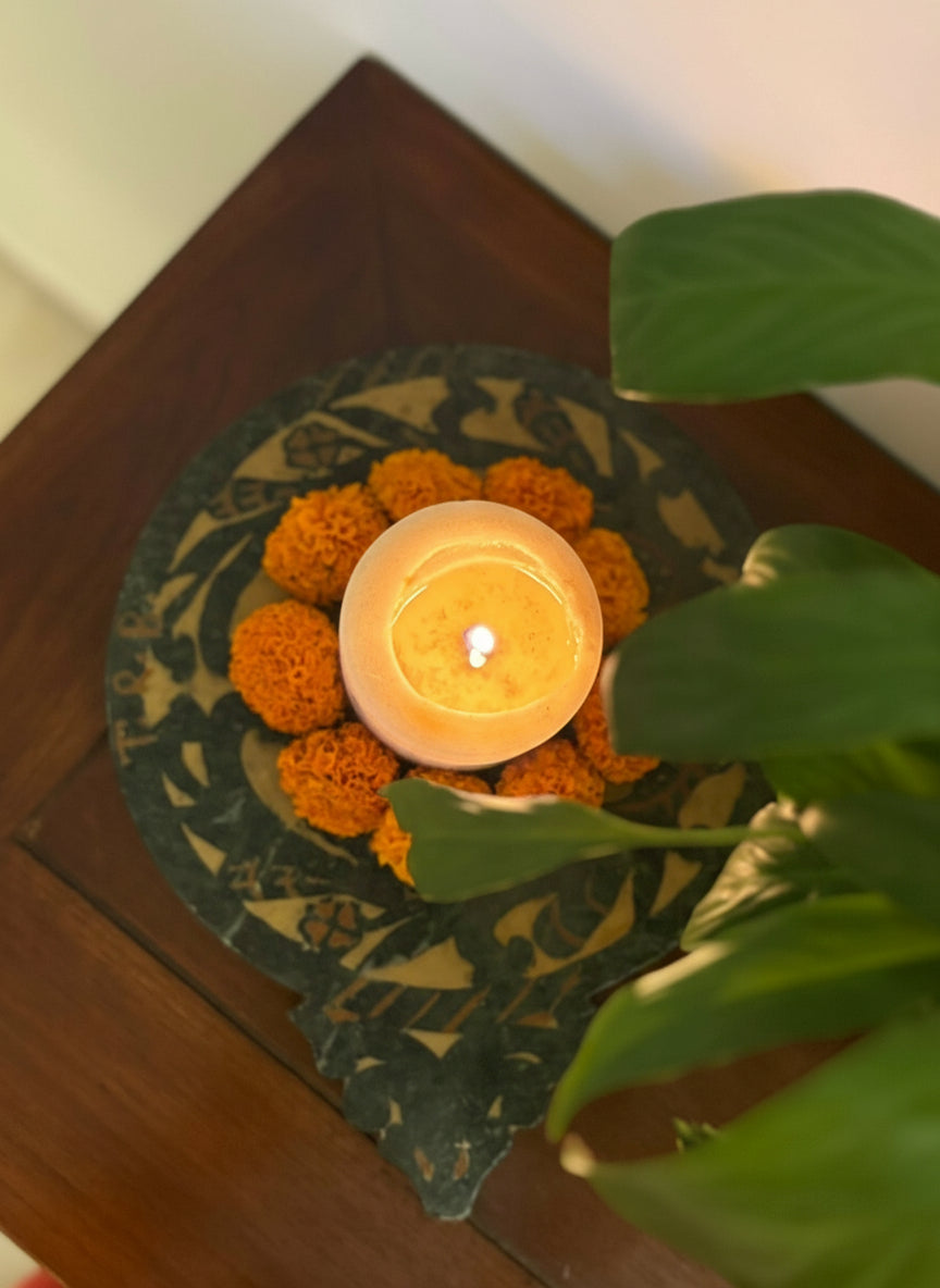 Candle holder surrounded by marigold flowers on a decorative mat with a plant in the foreground.