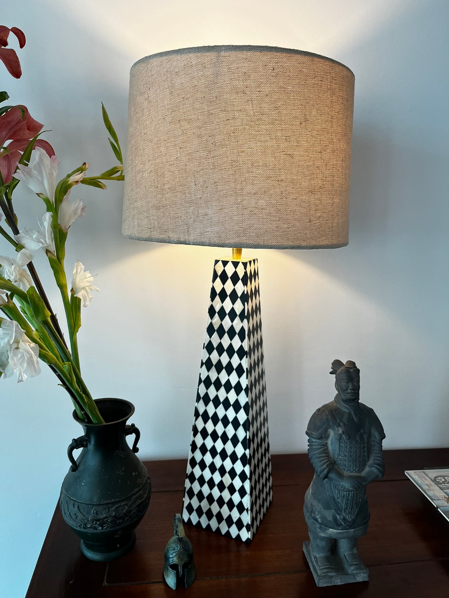 Hand-carved black and white checkered inlay lamp without a lampshade, placed on a table next to a potted plant and a decorative figure.