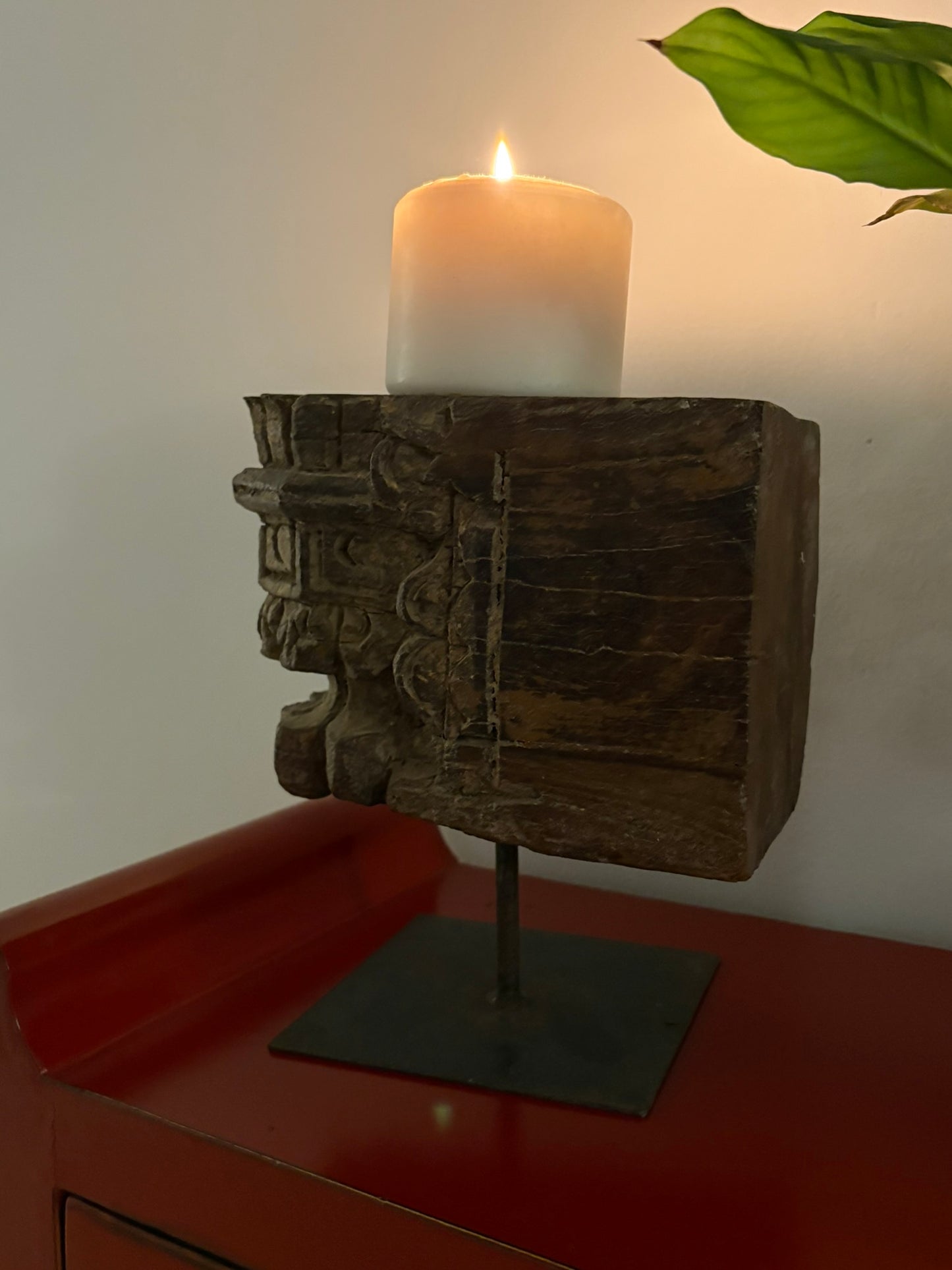 A vintage pillar candle base made of old teakwood, featuring ethnic motifs and hand-carved details, displayed on a metal stand.