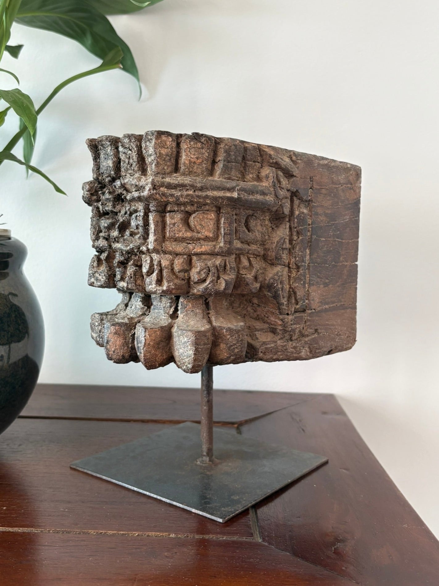 A vintage pillar candle base made of old teakwood, featuring ethnic motifs and hand-carved details, displayed on a metal stand.