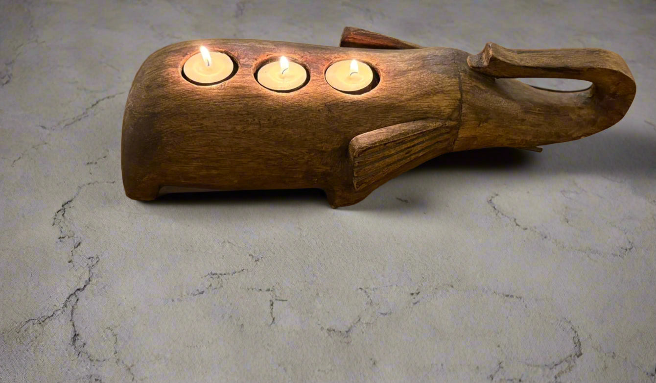 Wooden candle holder with elephant trunk handcarved with three lit candles on a marble surface