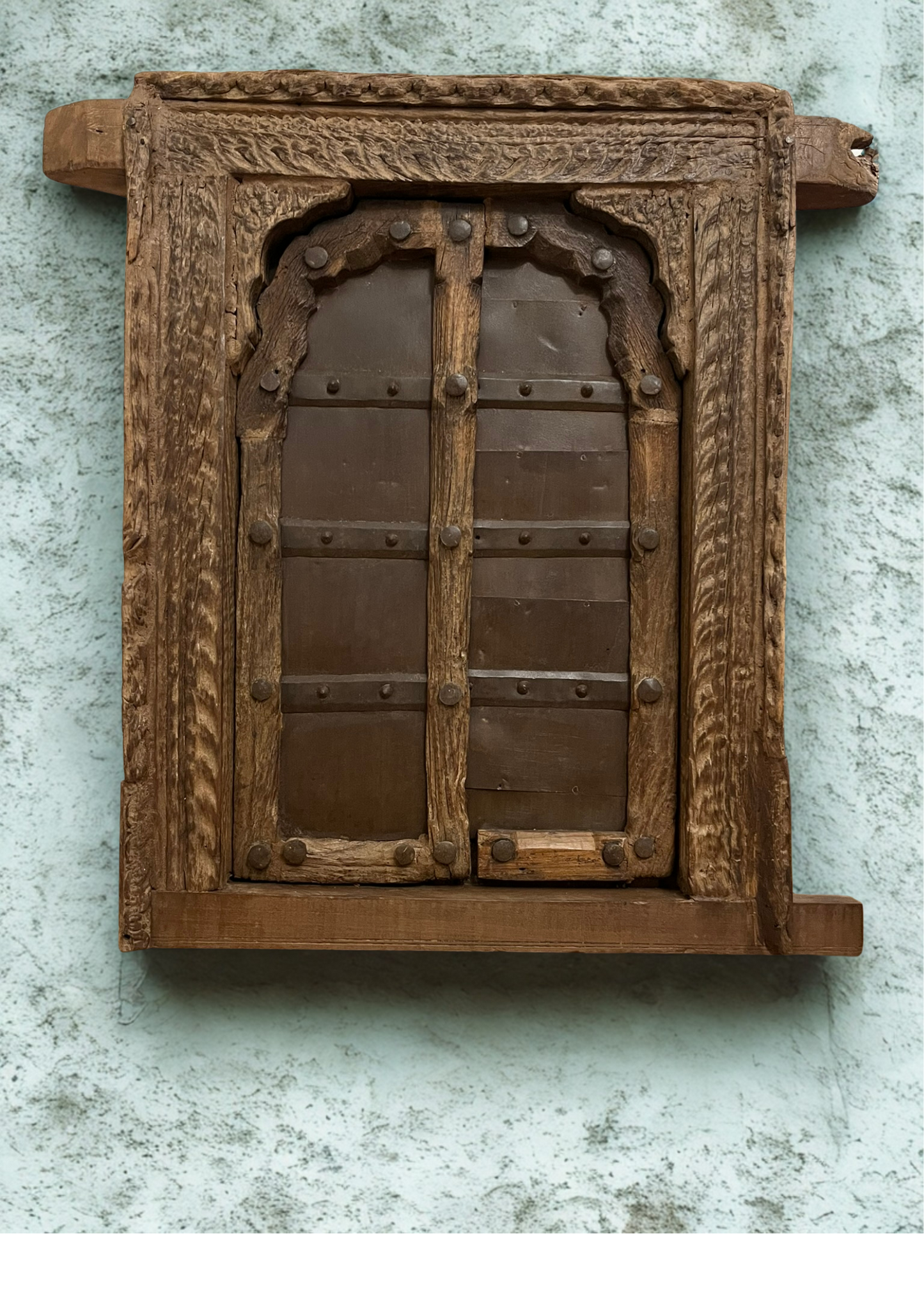 Wooden vintage window with intricate carvings on a textured wall.