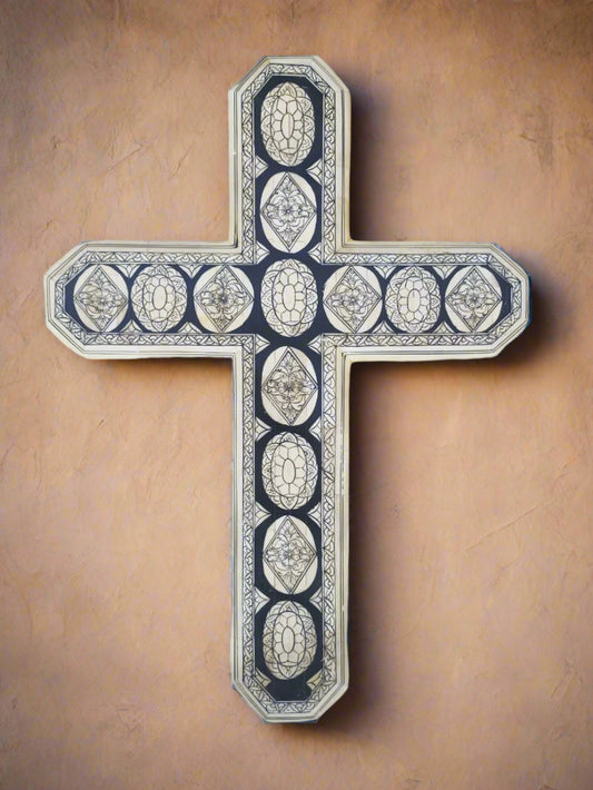 A hand painted cross with inlay design, made from wood and adorned with pieces of bone and resin, hanging on a wall.