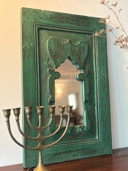 Green ornate vintage teakwood mirror  on a wooden surface