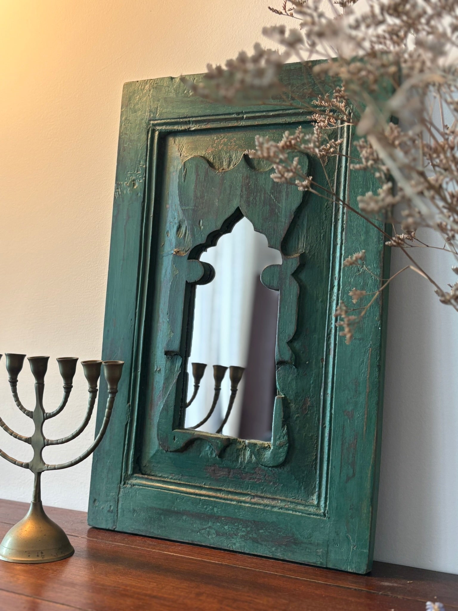 Vintage decorative mirror with a green frame on a wooden surface next to a Menorah.
