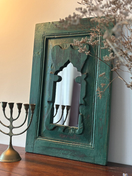 Vintage decorative mirror with a green frame on a wooden surface next to a Menorah.