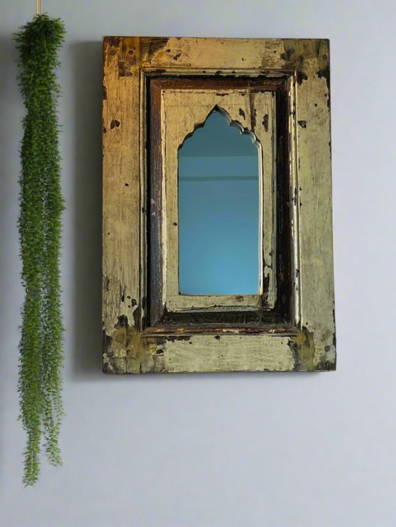 A vintage teakwood mirror with a decorative frame, hanging on a wall with a green decorative item to the left side.