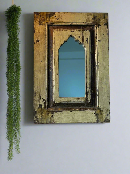 A vintage teakwood mirror with a decorative frame, hanging on a wall with a green decorative item to the left side.